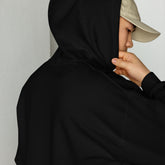 Black unisex hoodie close-up with drawstring hood and front pouch, hand holding collar