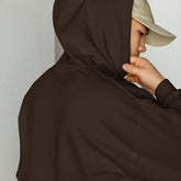 Brown unisex hoodie close-up with drawstring hood and front pouch, hand holding collar