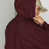 Maroon unisex hoodie close-up with drawstring hood and front pouch, hand holding collar
